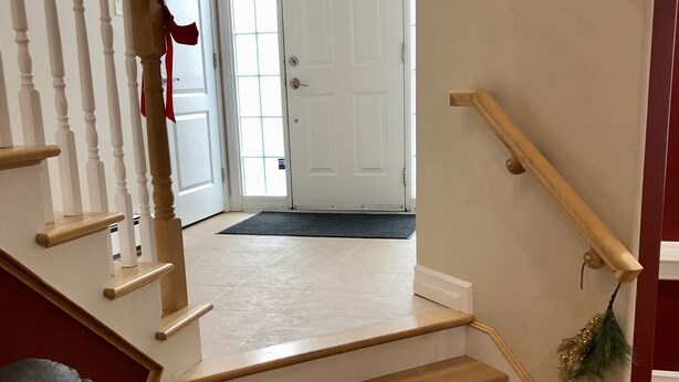A staircase with wooden steps and white walls, leading to a white door with a wreath.