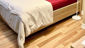 A neatly made bed with a red and white bedspread, a wooden headboard, and a white floor lamp beside it.
