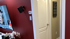 A hallway with red walls, a white door, and a black sign with text. There is a potted plant with white flowers on a black stand.