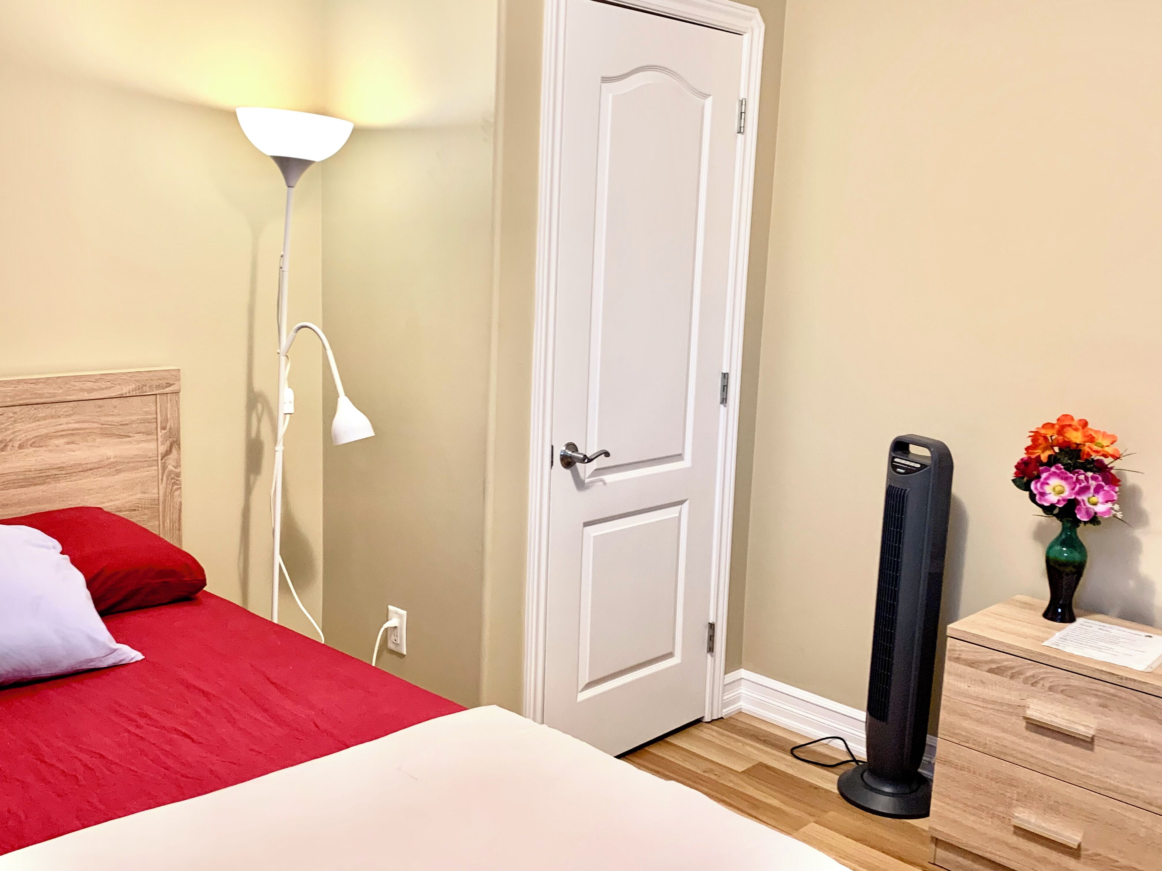 A bedroom with a bed, a bedside lamp, a dresser, a heater, and a vase with flowers.