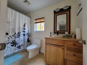Bathroom features a toilet, sink, and shower, with a cabinet for storage and a window for natural light.