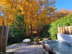 Relax on the deck with a hot tub and comfortable seating area surrounded by a lush lawn and autumn foliage.