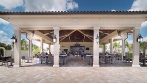 An outdoor patio with tables and chairs, a covered seating area, and a central bar. - Resort Style Living (Bradenton)