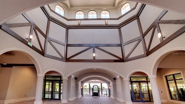 A spacious atrium with a high ceiling, multiple arches, and a central open area leading to a set of double doors. - Resort Style Living (Bradenton)