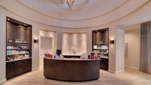 A modern reception area with a central counter, surrounded by shelves of toiletries and a decorative chandelier. - Resort Style Living (Bradenton)
