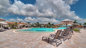 A pool area with lounge chairs and umbrellas, surrounded by palm trees and a clear sky. - Resort Style Living (Bradenton)