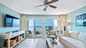 Un salon équipé d’un téléviseur, d’un canapé, d’une table basse et offrant une vue sur la plage grâce à de grandes portes vitrées.