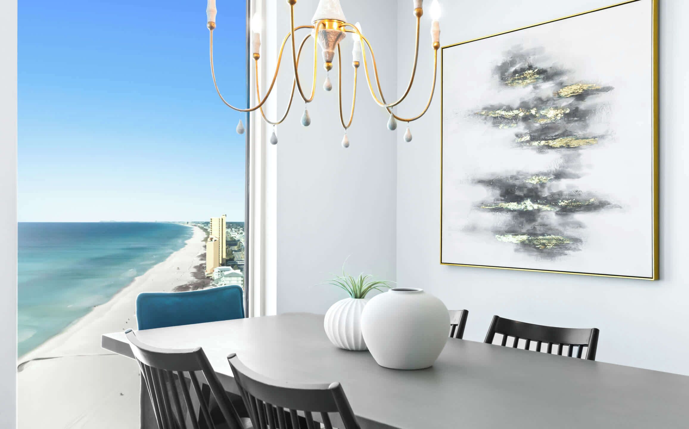 Un comedor con vista a la playa y al océano, un candelabro y un cuadro abstracto enmarcado.