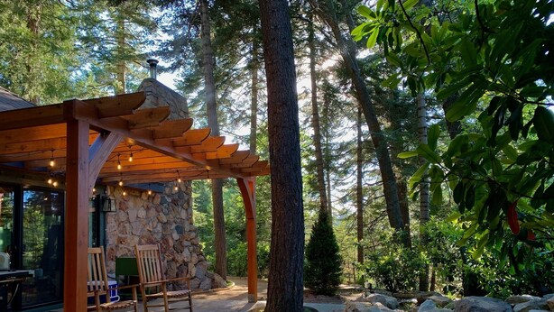 Una pérgola de madera con luces de cuerda, un muro de piedra y un área de estar con sillas y una mesa.