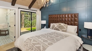 Un dormitorio con una cama grande, cabecera de madera y vistas a un jardín por medio de un ventanal.