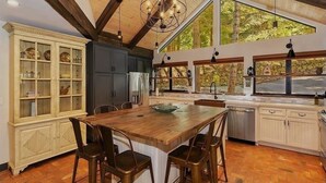 Una cocina amplia con una isla grande de madera, armarios oscuros y vistas al exterior a través de ventanas panorámicas.