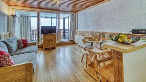 Ett mysigt vardagsrum med ett träpanelat tak, en soffa, en tv och en matplats med ett bord och stolar.