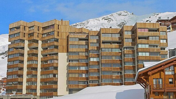 Ett hotell med flera våningar och balkonger, beläget med en snötäckt bergskedja som bakgrund.