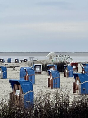 A beach with rows of blue beach chairs and umbrellas, some with wooden frames and others with metal frames, arranged on the sand. - Küstenbadeort Neßmersiel Nordseeküste (26553 Neßmersiel)