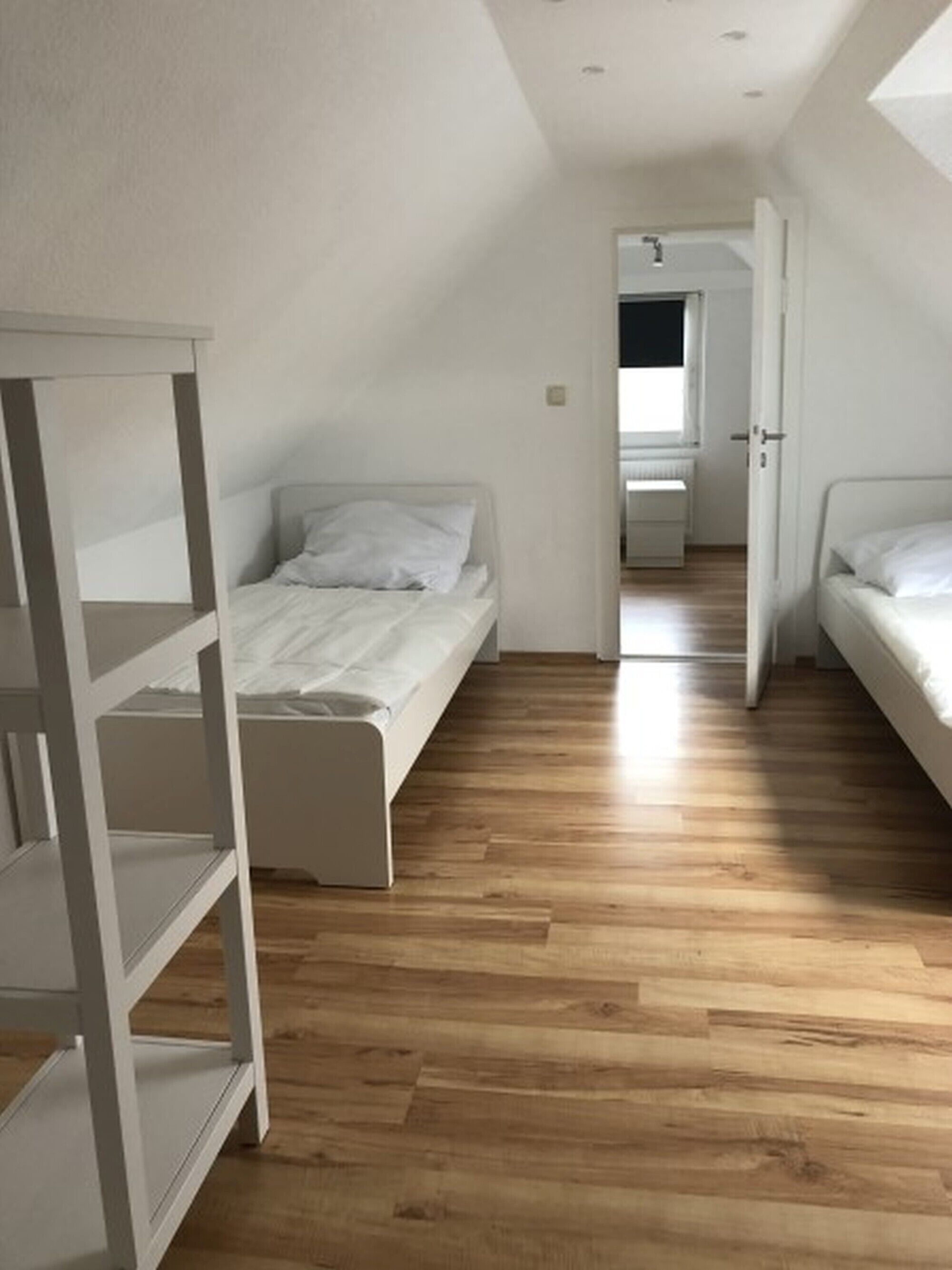 Un dormitorio con suelo de madera, una cama, un armario blanco y una puerta que da a otra habitación.