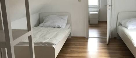 Un dormitorio con suelo de madera, una cama, un armario blanco y una puerta que da a otra habitación.