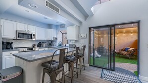 A modern kitchen with white cabinets, a large island with bar stools, a built-in microwave, and a coffee maker. - Private condo near Mayo Clinic with garage, patio, office, and pool access.  (Scottsdale)