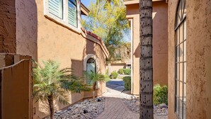 A narrow courtyard with a paved walkway, palm trees, and a building with a stucco exterior and large windows. - Private condo near Mayo Clinic with garage, patio, office, and pool access.  (Scottsdale)