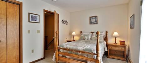 Une chambre à coucher avec un lit à baldaquin en bois, deux tables de chevet avec des lampes, une petite table de nuit et une porte donnant sur une autre pièce.