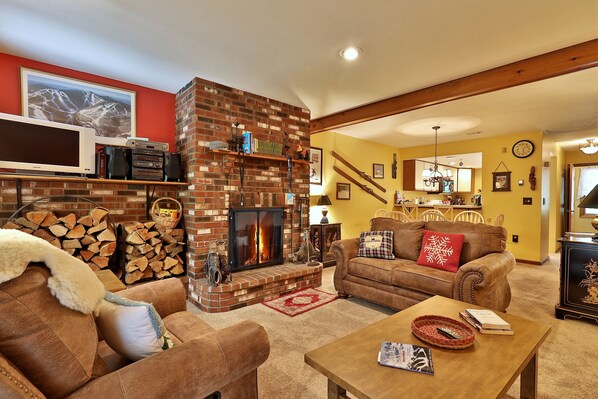 Una sala de estar acogedora con chimenea, televisor y un comedor al fondo.