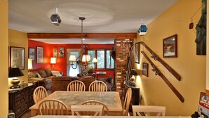 A dining area with a wooden table and chairs, a red accent wall, and a ski lift in the background. - Charming Glazebrook Condo - 1 Mile to Lifts - Close to everything! J3 (Killington)