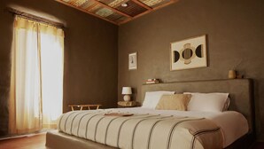 A bedroom with a large bed, a bedside table with a lamp, and a framed artwork on the wall. - Ghost Town Casitas — Casa Piedra & Desert Pearl together (Terlingua)
