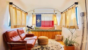 A cozy room with a leather sofa, a small ottoman, a flag, and a potted plant. - Ghost Town Casitas — Casa Piedra & Desert Pearl together (Terlingua)