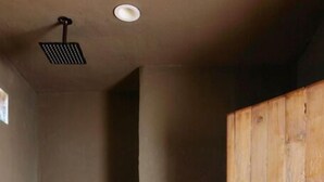 A room with a wooden door, a small shelf with bottles, a ceiling vent, and a concrete ledge. - Ghost Town Casitas — Casa Piedra & Desert Pearl together (Terlingua)