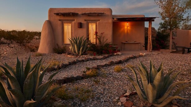 A stucco house with two doors, a small patio, and a garden with agave plants. - Ghost Town Casitas — Casa Piedra & Desert Pearl together (Terlingua)