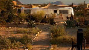 A caravan in a desert setting with a dirt path leading to it, surrounded by sparse vegetation and mountains in the background. - Ghost Town Casitas — Casa Piedra & Desert Pearl together (Terlingua)