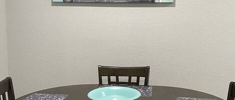 A dining area with a round table, chairs, and a painting of a pier leading to the sea.