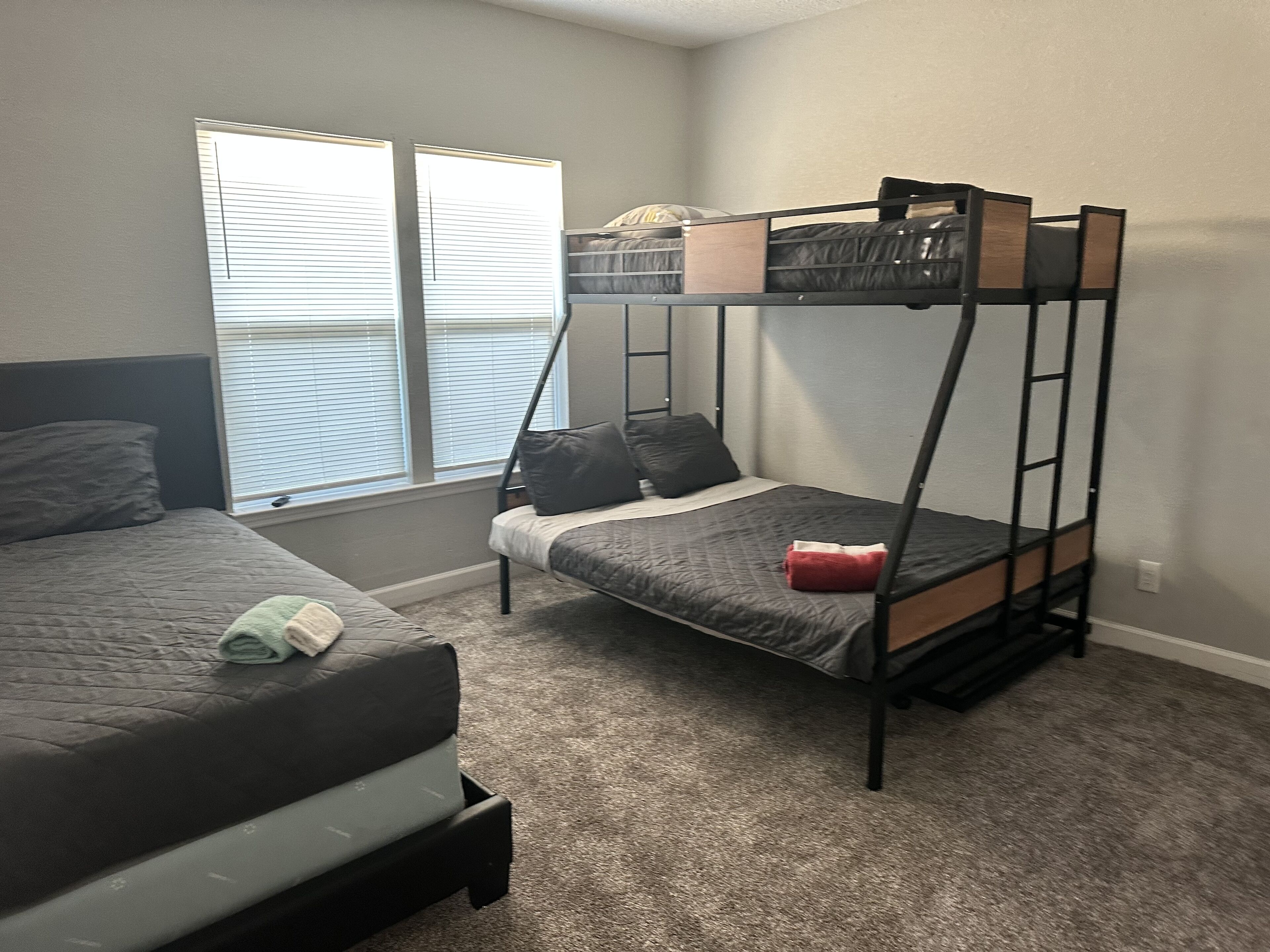 Quarto com duas beliches, uma janela com cortinas e piso coberto por carpete.