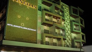 Un hotel de varios pisos con un letrero llamativo que dice "The Venetian Hotel, Banquets, Lawns, Restaurant".