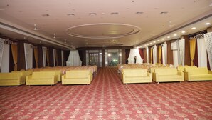 Un amplio salón con hileras de sofás amarillos y una alfombra estampada, con un techo alto que cuenta con iluminación empotrada y elementos decorativos.