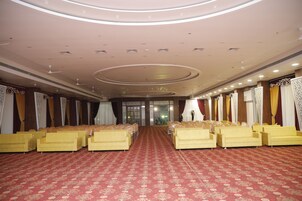 Un amplio salón con hileras de sofás amarillos y una alfombra estampada, con un techo alto que cuenta con iluminación empotrada y elementos decorativos.