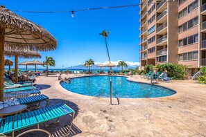 Un espace piscine équipé de chaises longues, de parasols et d’un bâtiment doté de balcons.