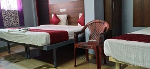 A hotel room with two beds, a wooden headboard, a red chair, and a patterned curtain. - Skyry hotels Iyyappathangal (Chennai)