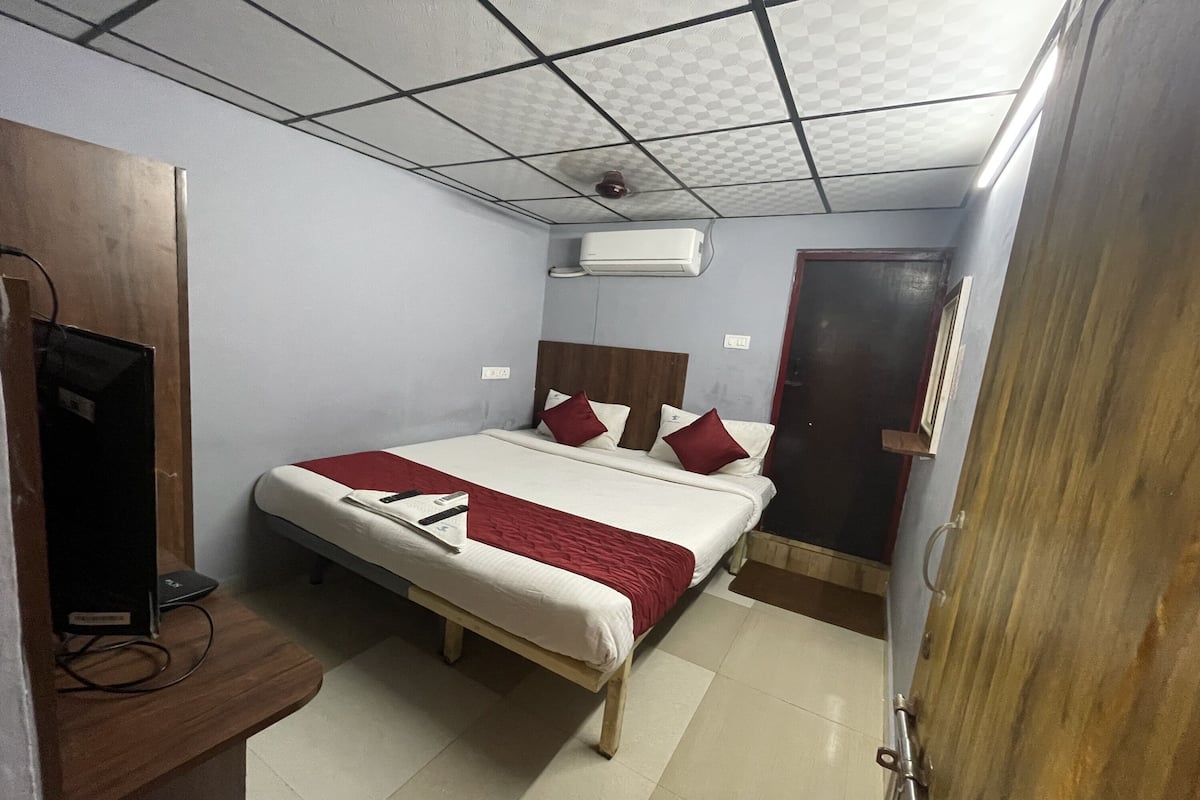 Quarto de hotel com cama, escrivaninha com computador, aparelho de ar condicionado e uma porta.