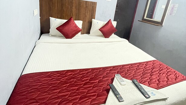 Habitación de hotel con una cama, almohadas, una manta roja y dos controles remotos.