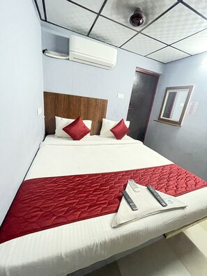 A hotel room with a bed, pillows, a red blanket, and two remote controls. - Skyry hotels Iyyappathangal (Chennai)