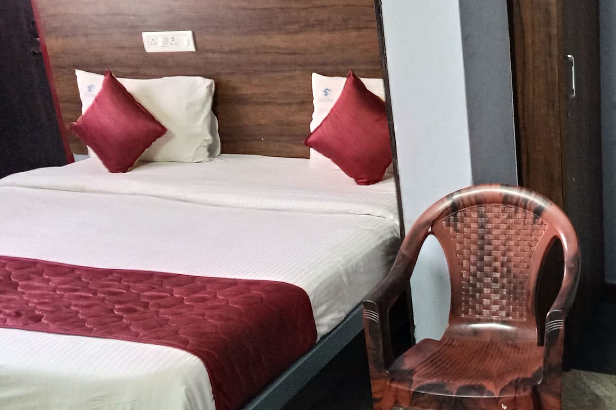 Quarto de hotel com duas camas, cada uma com almofada vermelha e branca, e cabeceira de madeira.