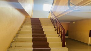 Una escalera con peldaños alternados de colores oscuros y claros, barandilla de madera y una lámpara en el techo.