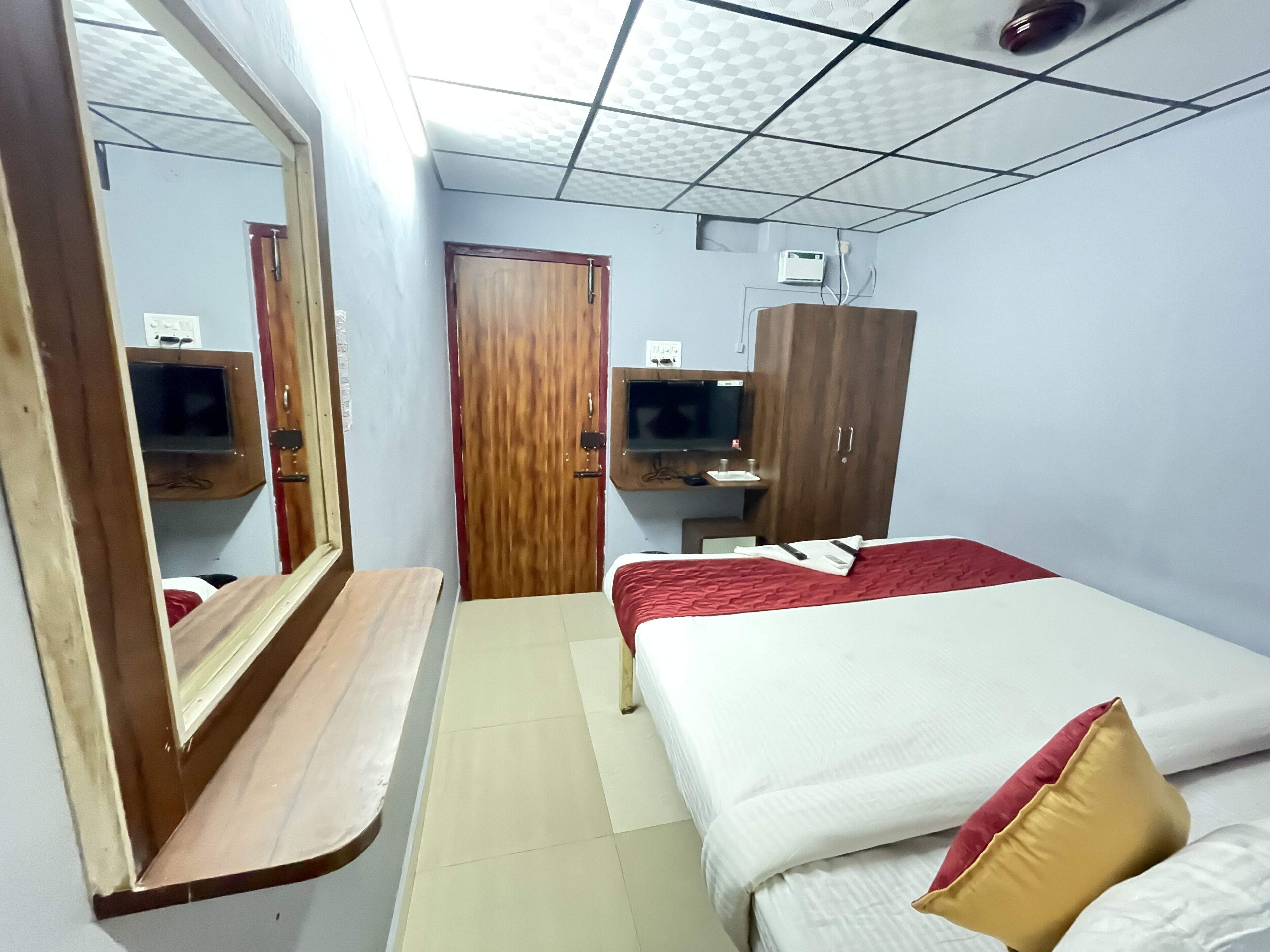 A bedroom with a wooden wardrobe, a bedside table, a bed with red and white bedding, and a mirror.