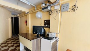 Una zona de recepción con piso a cuadros, un escritorio con computadora, un ventilador y un extintor.