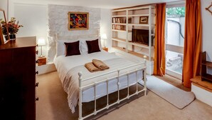 A bedroom with a white bed, a stone wall, a bookshelf, and a window with curtains.