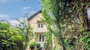 A stone house with a gabled roof, surrounded by dense greenery and trees.