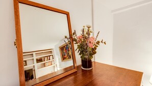 A wooden table with a mirror, a vase with flowers, and a framed picture on the wall.