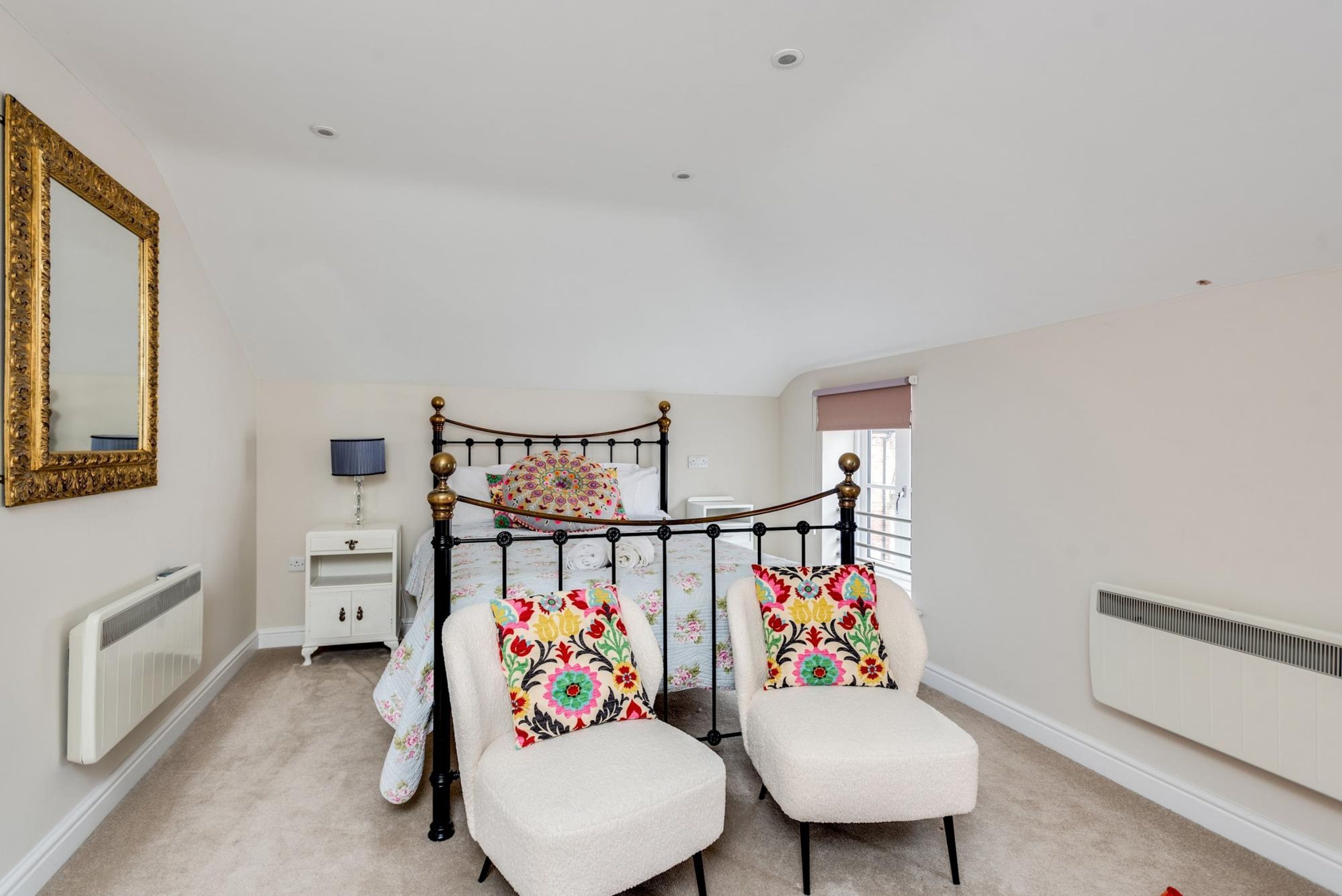 A bedroom with a four-poster bed, two chairs, a nightstand, a lamp, and a radiator.