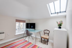A room with a desk, chair, TV, radiator, window with blinds, and a skylight. - The Mews - 1BR Studio in Jericho Near City Centre (Oxford)
