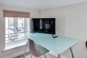Un espacio de oficina moderno con un escritorio de vidrio, una silla, un televisor de pantalla plana y una ventana con vista a la calle.